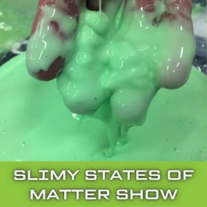 A hand is lifting up green cornflour slime and slime is dripping off the fingers and into a bowl.