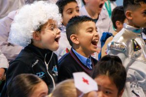 An audience of children watching a science show and looking surprised. Two boys are laughing.